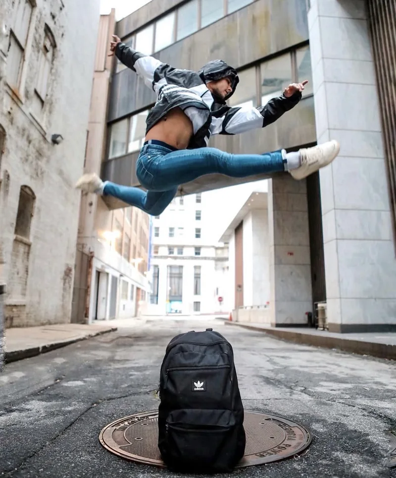 A dancer in a split leap above a backpack in a city alley