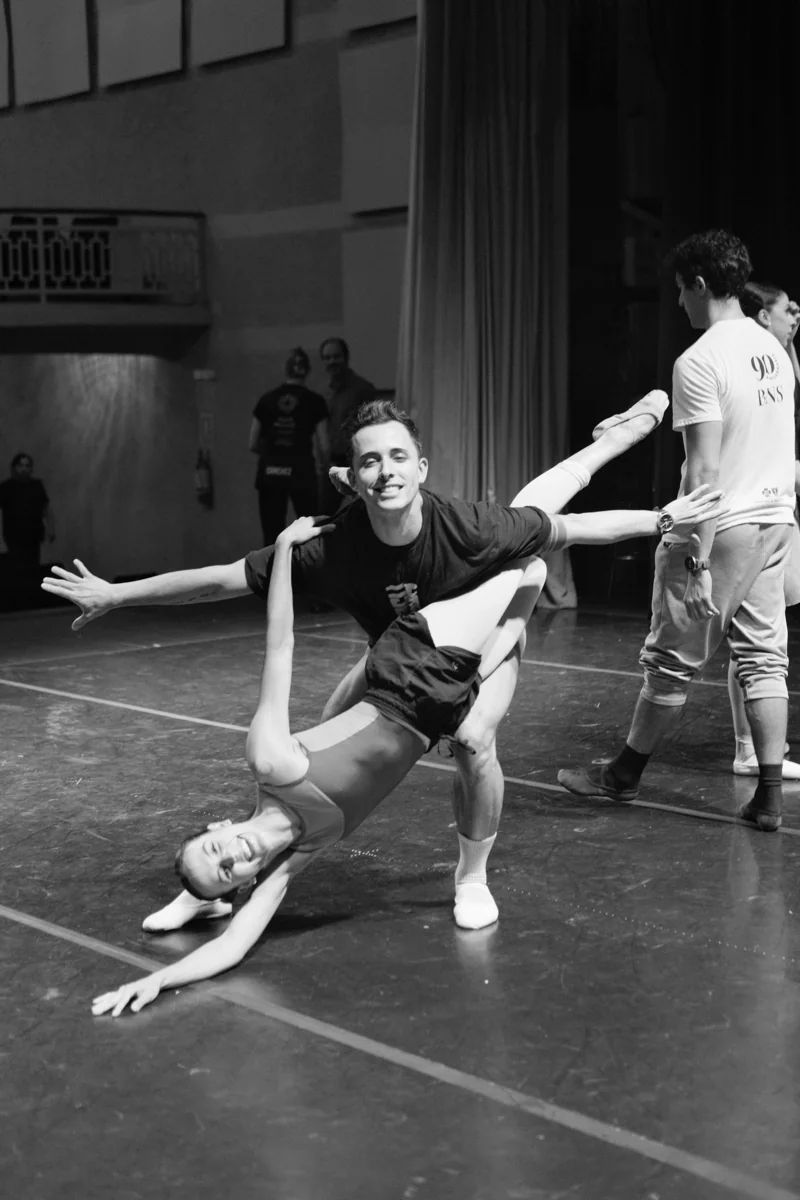 A black-and-white image of a playful supported duet in rehearsal